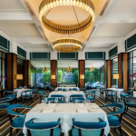 Luxurious restaurant interior with teal‑blue chairs, striped flooring, and golden chandeliers, offering modern fine dining ambiance surrounded by large windows and natural light.