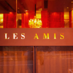 Elegant exterior of Les Amis fine dining restaurant in Singapore with warm golden lighting, red interior tones, and chandelier reflections, showcasing a luxurious French dining ambiance.