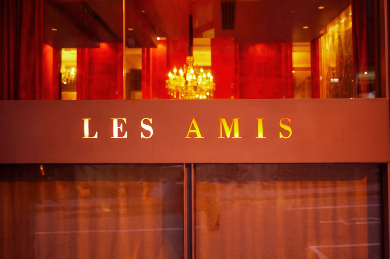 Elegant exterior of Les Amis fine dining restaurant in Singapore with warm golden lighting, red interior tones, and chandelier reflections, showcasing a luxurious French dining ambiance.