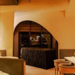 Elegant fine‑dining restaurant interior in Singapore featuring warm amber lighting, curved architecture, and modern booth seating with a view into the open kitchen.