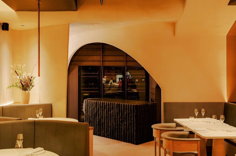 Elegant fine‑dining restaurant interior in Singapore featuring warm amber lighting, curved architecture, and modern booth seating with a view into the open kitchen.