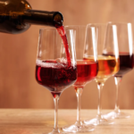 Red wine being poured into a glass beside rosé and white wine — elegant wine tasting setup on wooden table.