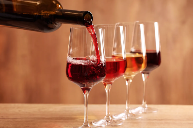 Red wine being poured into a glass beside rosé and white wine — elegant wine tasting setup on wooden table.