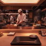 Japanese chefs in white uniforms preparing dishes behind a wooden omakase counter at a fine‑dining restaurant in Singapore, showcasing traditional culinary precision.