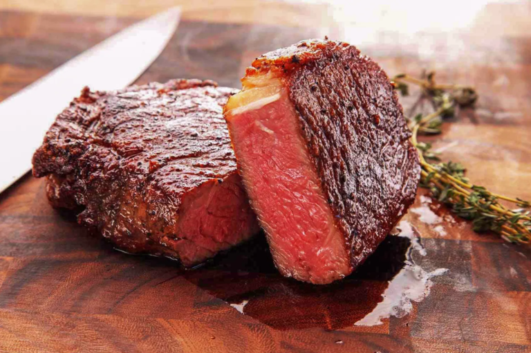 Juicy medium‑rare steak with seared crust on wooden cutting board beside knife and thyme — premium beef cooked to perfection.