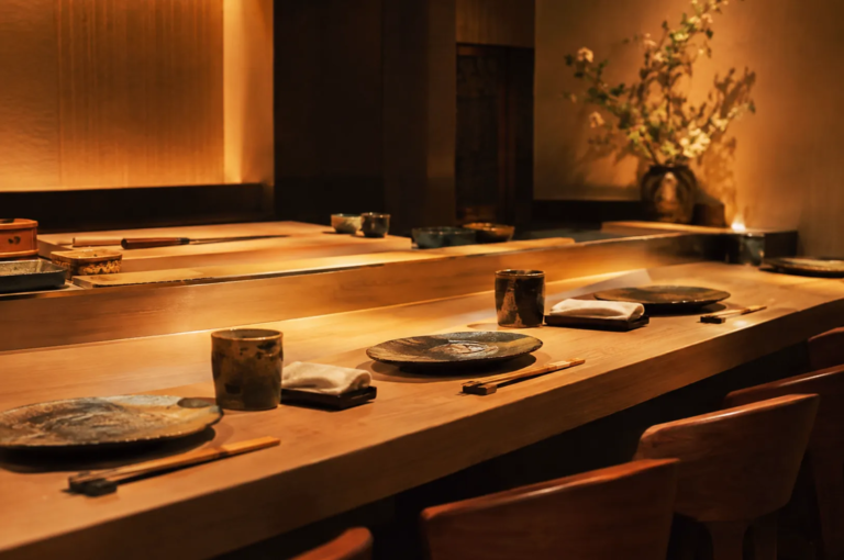 Elegant Japanese omakase counter with handcrafted ceramic plates, wooden chopsticks, and warm ambient lighting creating a refined fine‑dining atmosphere.