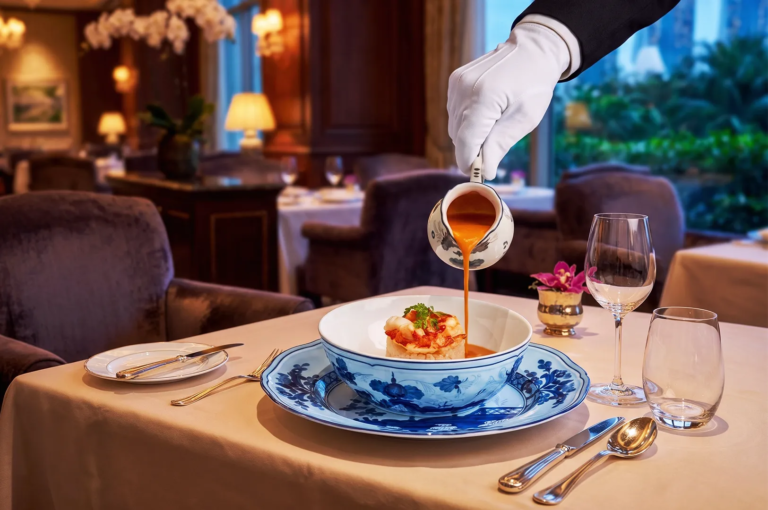 Elegant fine dining table setting with a waiter pouring rich lobster bisque into a porcelain bowl — upscale restaurant experience in Singapore.