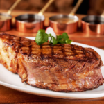 Juicy ribeye steak with perfect grill marks served on a white plate, garnished with herbs and sauces in copper pots in the background; premium steakhouse presentation.