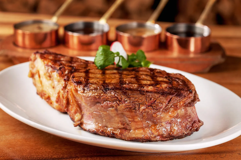 Juicy ribeye steak with perfect grill marks served on a white plate, garnished with herbs and sauces in copper pots in the background; premium steakhouse presentation.