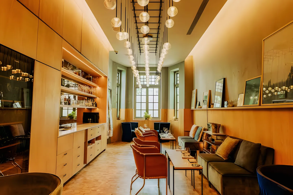 Modern lounge interior with warm lighting, wooden shelves stocked with glassware and bottles, and cozy seating featuring cushioned chairs and sofas. Pendant lights hang in symmetrical rows, creating a sophisticated atmosphere ideal for upscale dining or cocktails in Singapore.