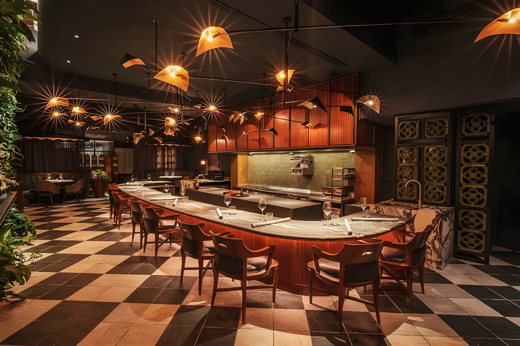 High‑end restaurant with marble chef’s counter, golden pendant lights, and checkered flooring, combining modern architecture with warm lighting.
