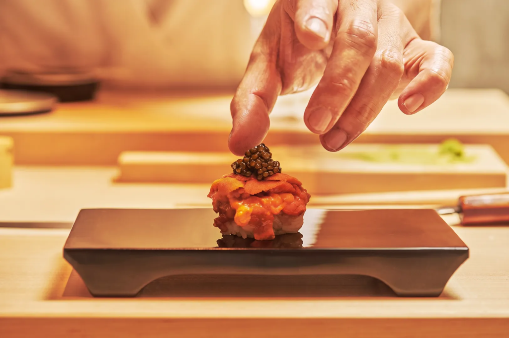 Chef garnishing uni sushi with caviar at a luxury omakase restaurant, highlighting precision and artistry.