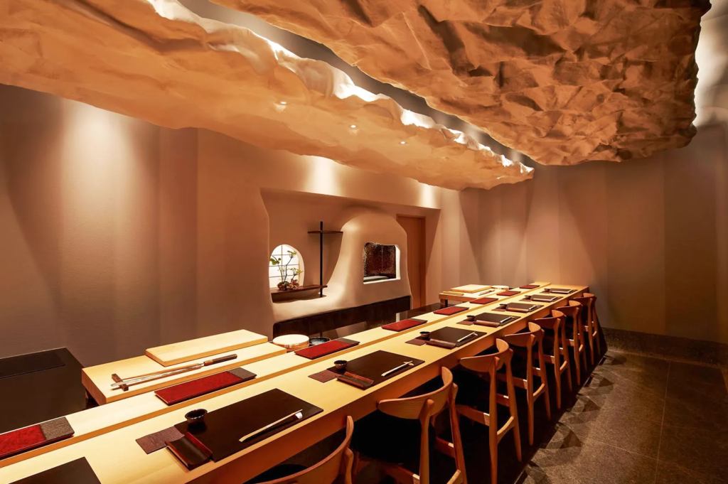 Japanese fine‑dining interior featuring sculpted ceiling and minimalist sushi counter with warm lighting.