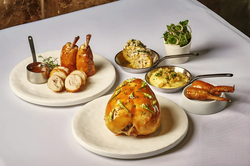Gourmet roasted chicken served with creamy sides, corn, and salad on white ceramic plates, highlighting refined plating and culinary craftsmanship.
