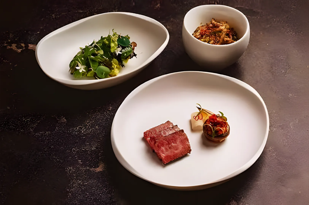 Gourmet plated dishes at a Michelin‑style restaurant in Singapore showcasing seared beef, fresh greens, and artistic modern plating on minimalist white ceramics.