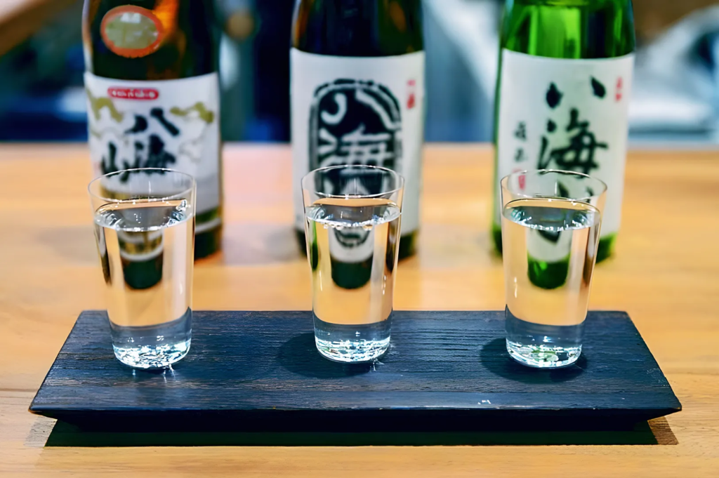 Sho Chiku Bai premium sake bottle surrounded by crystal glasses and bar accessories on a wooden table — refined Japanese sake presentation for luxury dining.