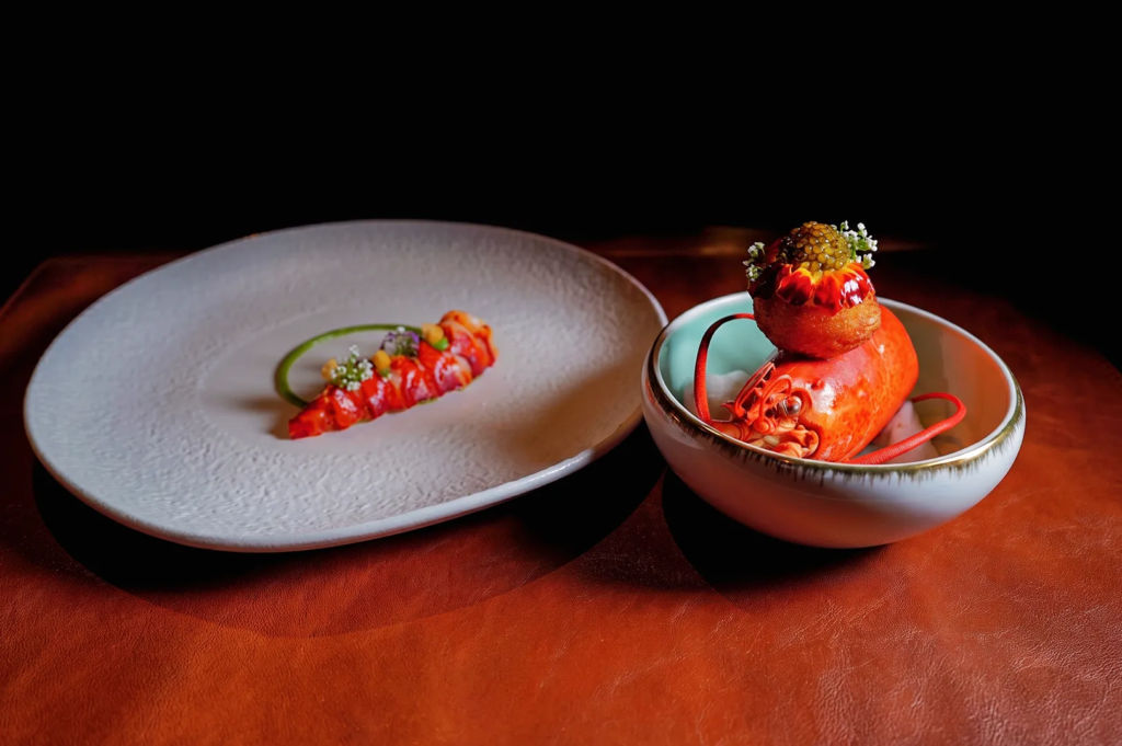 Artfully plated lobster dish with vibrant red tail and caviar garnish served on textured plates at Les Amis Singapore, representing exquisite French haute cuisine presentation.