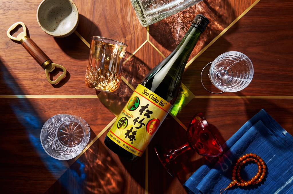 Hakushika Junmai Ginjo sake bottle with gold and black label on a tray beside ceramic cups and cherry blossoms — elegant Japanese sake scene with traditional decor.