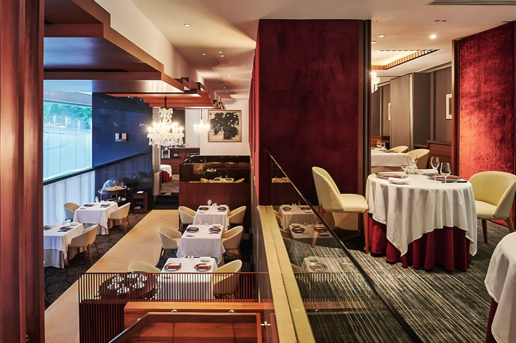 Upscale restaurant with crystal chandeliers, red velvet walls, and white‑clothed tables arranged across two levels, creating a sophisticated dining atmosphere.