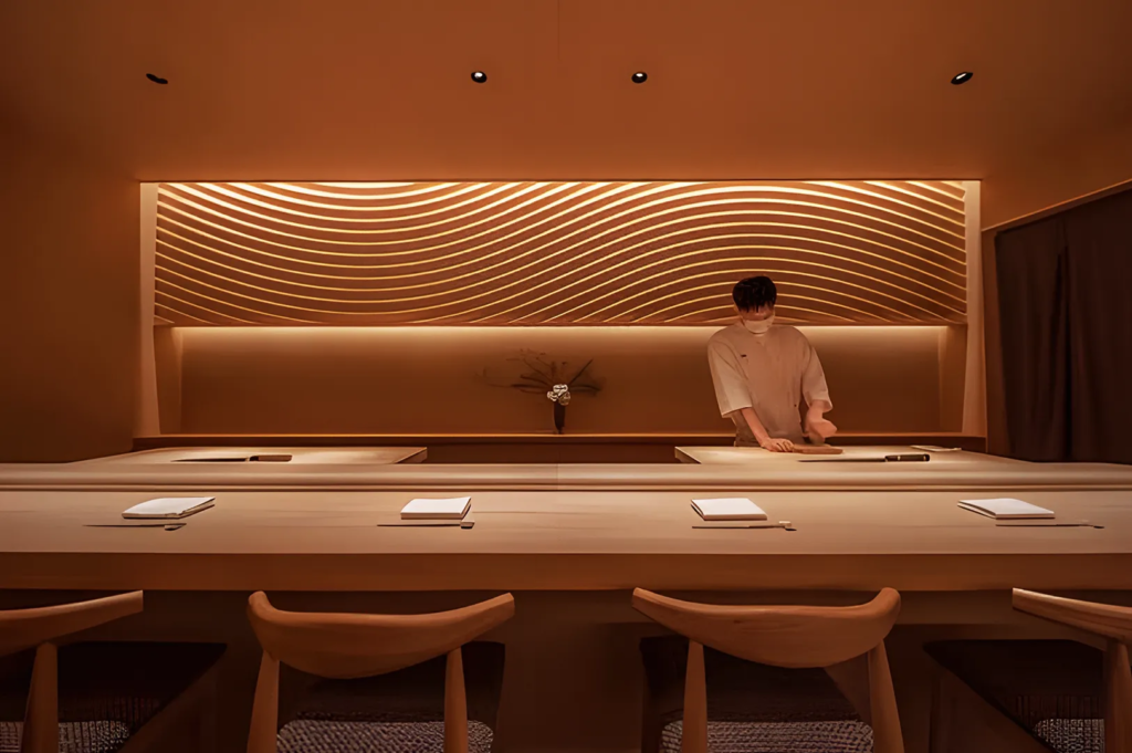Contemporary omakase sushi counter with wave‑pattern wall and warm lighting, showcasing Japanese craftsmanship and design.