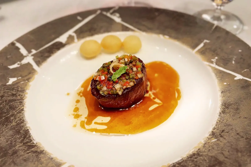 Tender beef fillet topped with diced vegetables and rich sauce on a designer plate at Les Amis Singapore, showcasing refined French culinary craftsmanship.