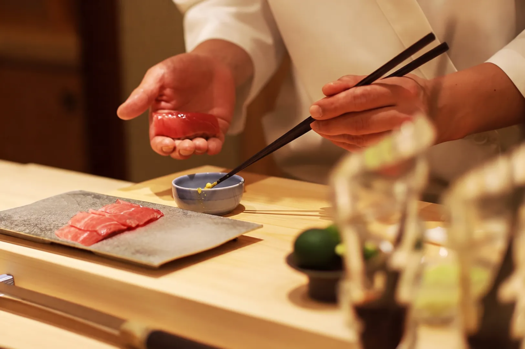 Japanese sushi chef preparing fresh tuna nigiri with wasabi at a fine‑dining omakase counter in Singapore.
