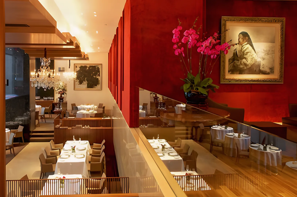 Luxurious interior of Les Amis Singapore featuring red walls, chandeliers, orchids, and framed artwork, creating a sophisticated fine dining atmosphere.
