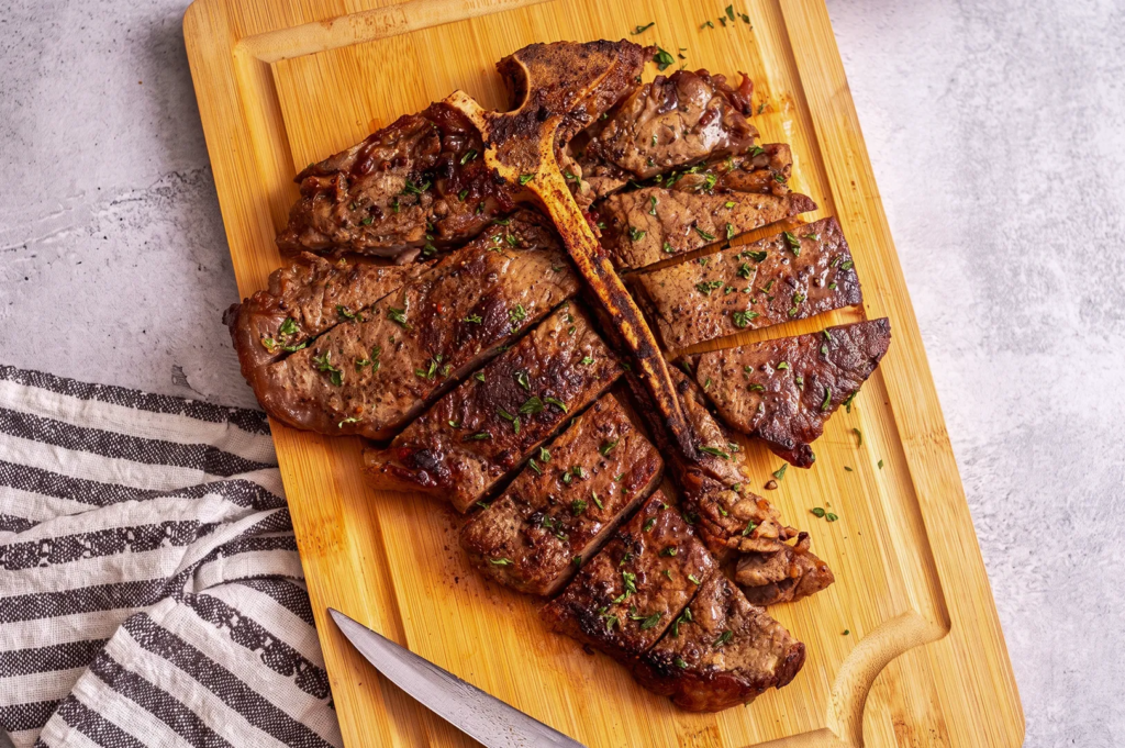 Juicy porterhouse steak sliced and garnished with herbs on a wooden board; classic steakhouse serving style.