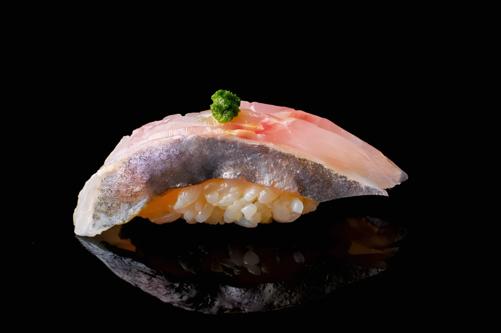 Close‑up of premium sushi topped with silver fish and wasabi garnish on glossy black background at a luxury Japanese restaurant.