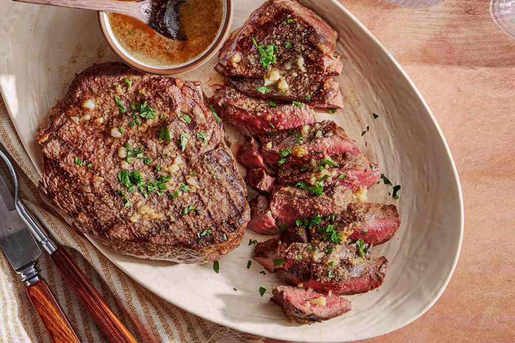 Medium‑rare sirloin steak sliced and topped with garlic butter and herbs, served with dipping sauce; elegant home‑cooked presentation.