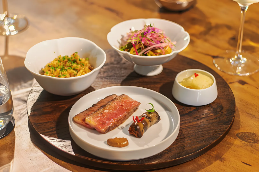 Elegant tasting platter with seared beef, risotto, salad, and creamy side dishes served on white ceramic plates, showcasing refined culinary presentation.