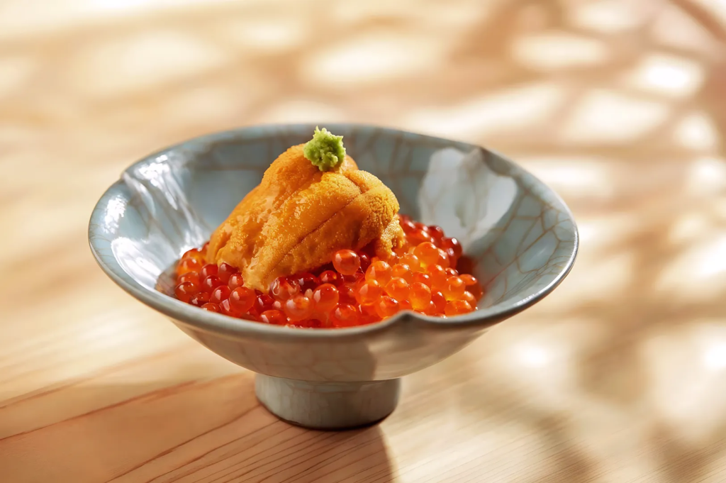 Sea urchin and salmon roe served in a ceramic bowl with wasabi garnish at a high‑end Japanese restaurant.