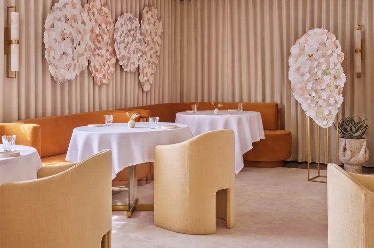 Sophisticated restaurant interior with beige and caramel tones, round tables draped in white linens, and artistic wall installations, showcasing modern luxury dining ambiance.
