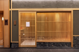 Elegant Japanese restaurant exterior in Singapore featuring wooden lattice doors, stone base accents, and warm ambient lighting that highlights minimalist architecture.