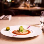 Elegant fine‑dining dish served at a luxury restaurant in Singapore featuring scallop carpaccio with tomato sauce, microgreens, edible flowers, and lime garnish on a marble table.