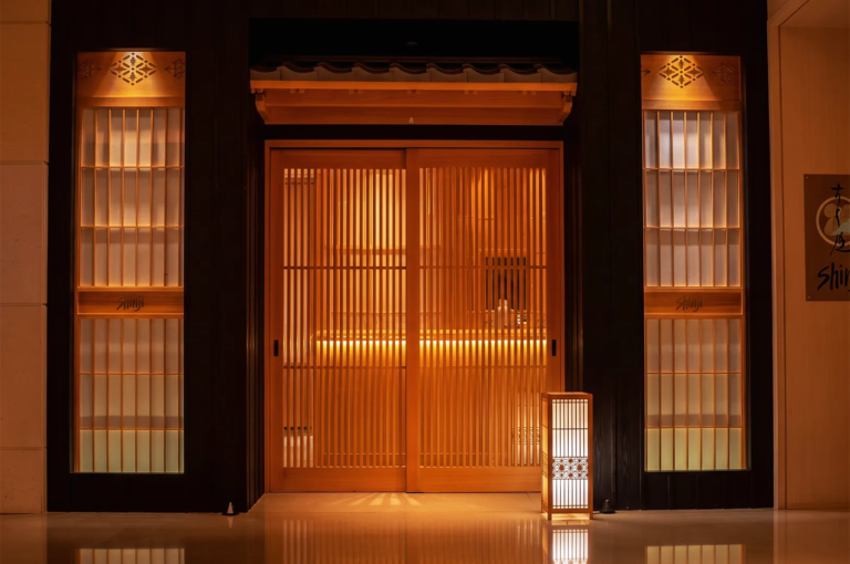 Elegant entrance of Shinji Japanese restaurant in Singapore featuring traditional wooden sliding doors, warm lighting, and minimalist Japanese architecture.