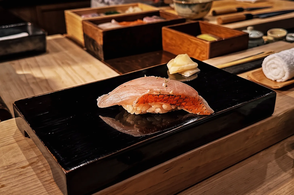 Fresh kinmedai red sea bream nigiri sushi served on a black lacquer serving board.