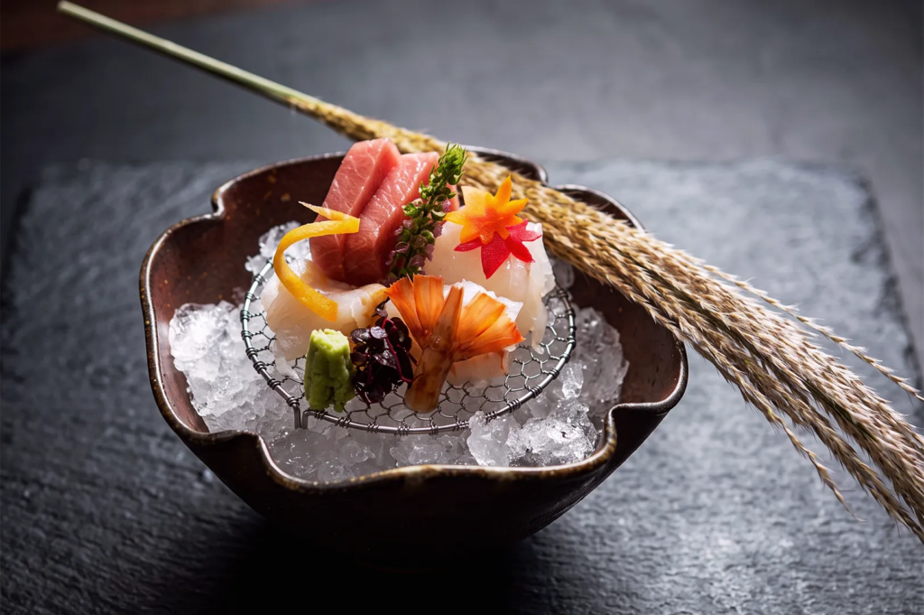Artistic sashimi platter with tuna, shrimp, and white fish on crushed ice, garnished with edible flowers and herbs — premium Japanese cuisine presentation.