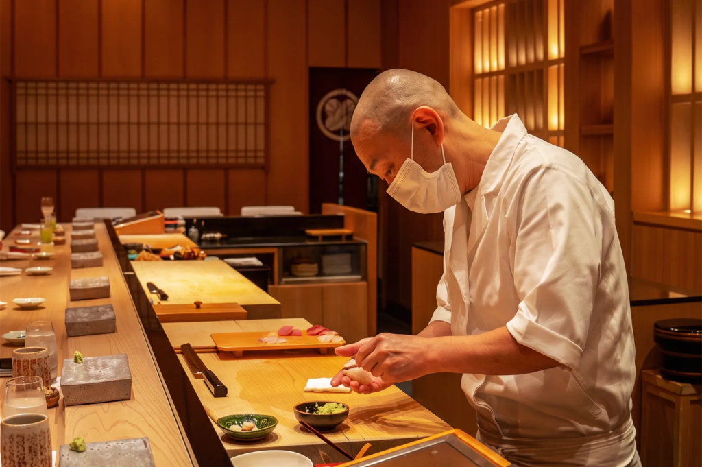 Sushi chef at Shinji Singapore carefully crafting nigiri behind a wooden counter in an intimate omakase dining setting.