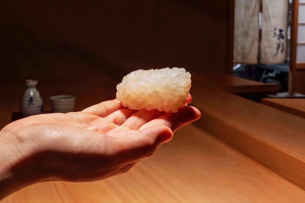 Close‑up of perfectly shaped sushi rice held in hand at a Japanese sushi bar, highlighting texture, precision, and craftsmanship in authentic sushi preparation.