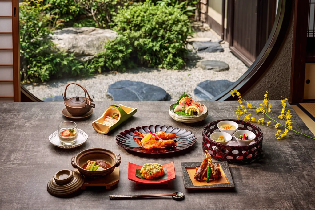 Elegant kaiseki meal with assorted Japanese dishes including sashimi, tempura, and soup served beside a garden view — authentic fine dining experience.