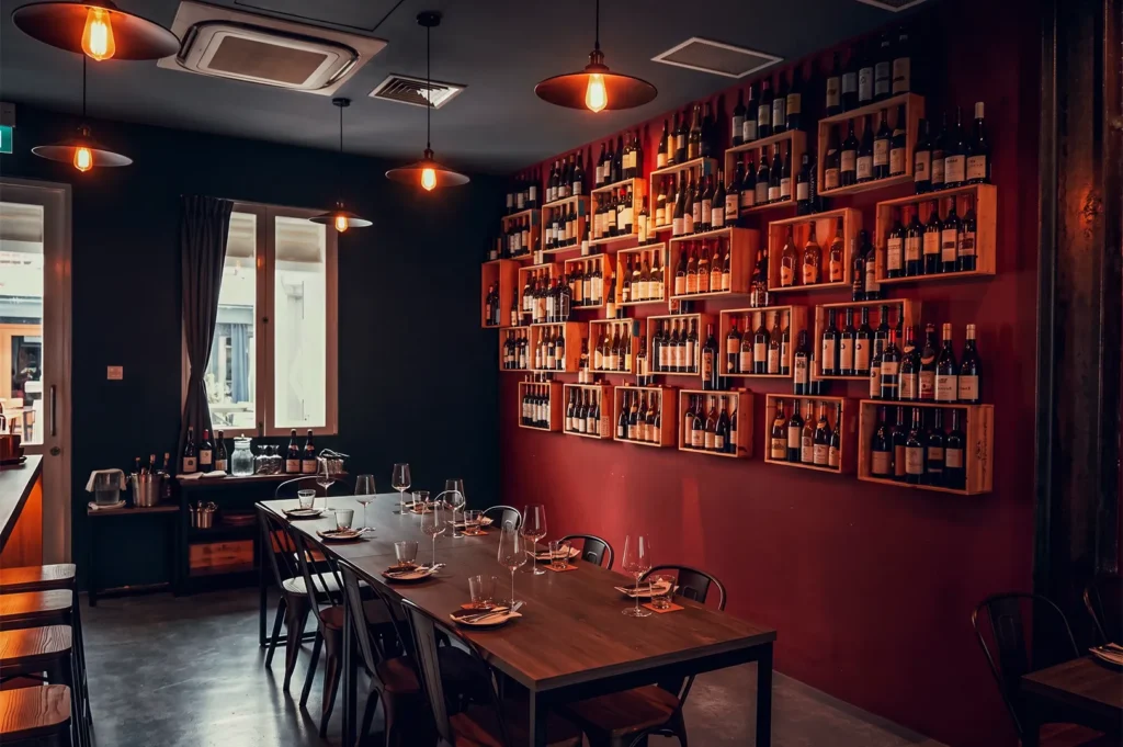 Cozy wine dining room in Singapore with warm lighting, deep red walls, and shelves filled with wine bottles creating an intimate atmosphere.