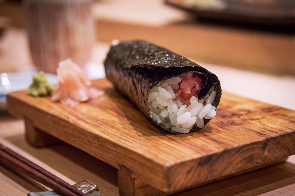 Traditional sushi hand roll with tuna and rice wrapped in seaweed, served with pickled ginger and wasabi at Shinji Singapore.
