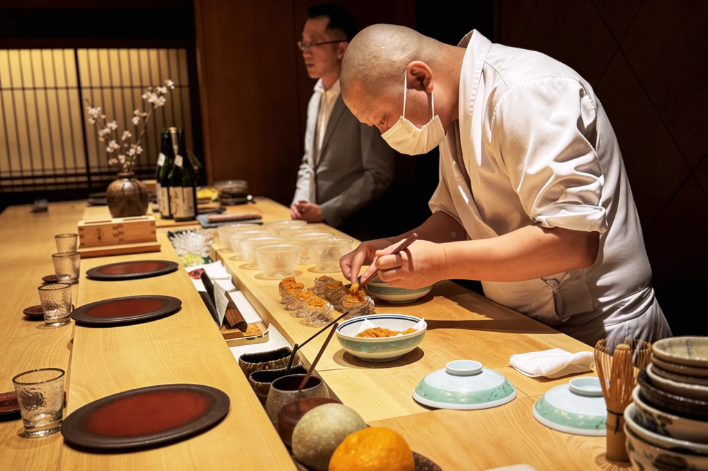 Sushi chef plating fresh uni at a wooden counter in a luxury Japanese restaurant, emphasizing culinary artistry and attention to detail in omakase dining.