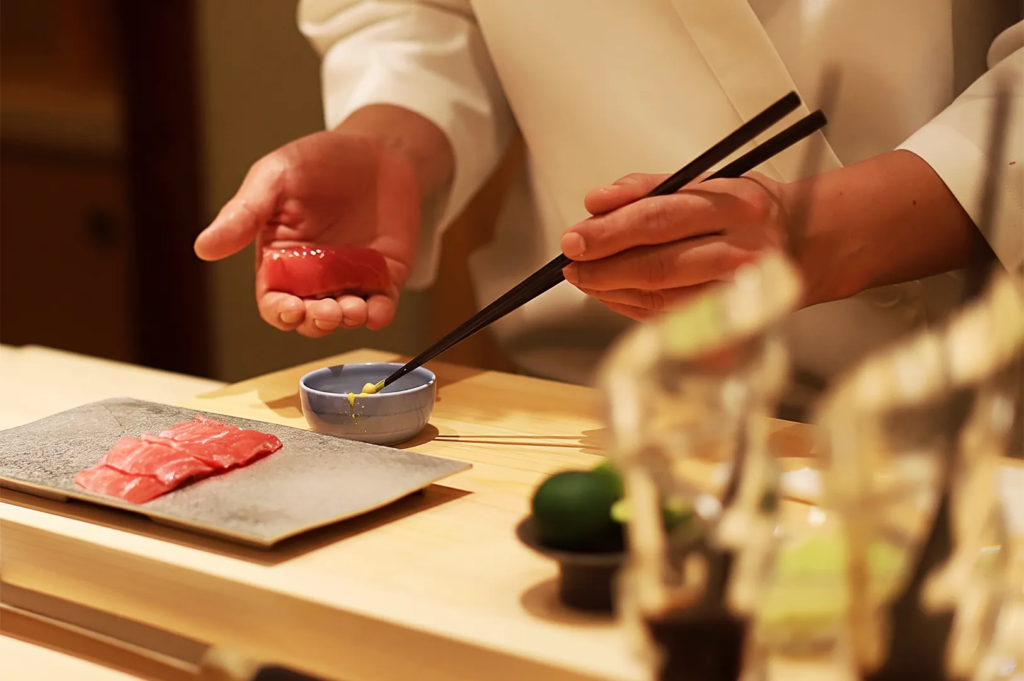 Sushi chef plating fresh tuna nigiri with chopsticks at a refined omakase counter, highlighting precision and artistry in Japanese fine dining.