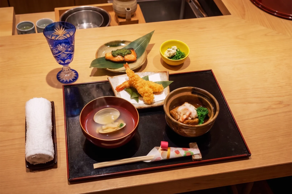 Japanese multi‑course meal featuring tempura shrimp, soup, grilled fish, and side dishes on lacquer tray — refined kaiseki presentation.