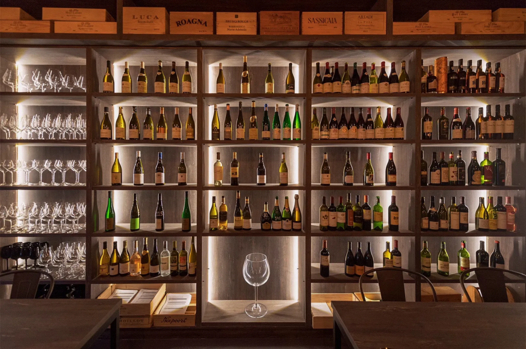 Elegant wine cellar in Singapore restaurant with illuminated shelves displaying premium wine bottles, glassware, and wooden crates for storage.