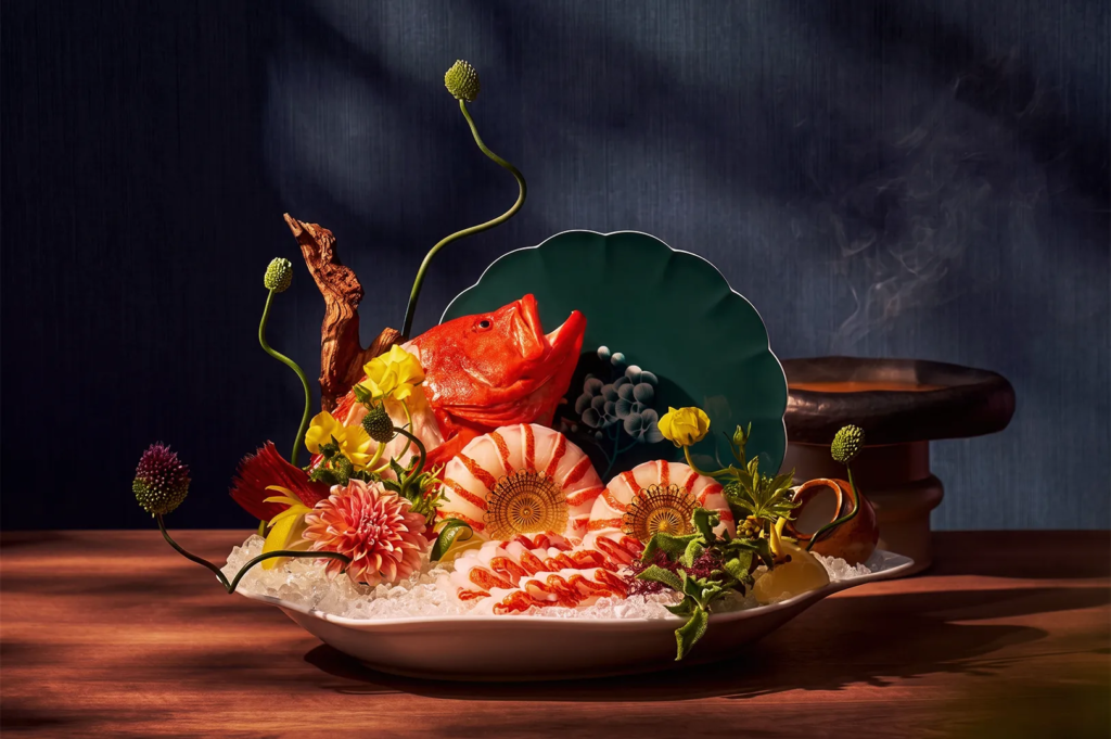 Exquisite Japanese seafood presentation featuring a red fish head, shrimp, and sashimi slices arranged on ice with vibrant flowers and greenery, symbolizing luxury Japanese dining.